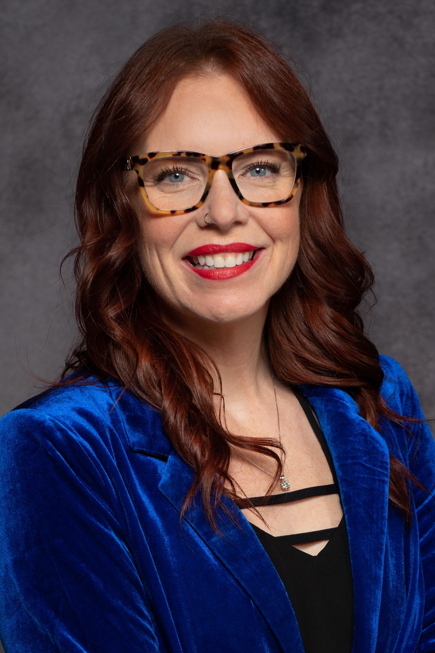 Professional headshots showing a dark-haired figure in glasses and a royal blue velvet jacket against a grey background.