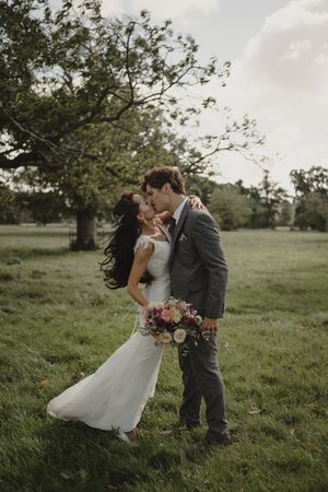 Newlyweds embracing in a romantic outdoor meadow setting with soft natural lighting.