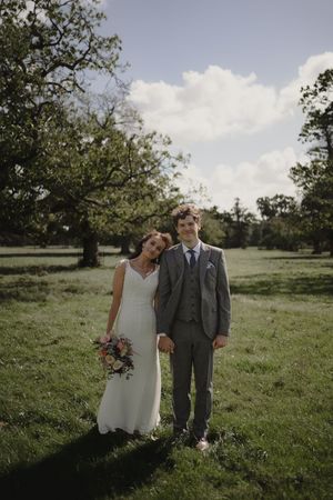 Wedding couple posing together in a sunlit meadow with trees in the background.