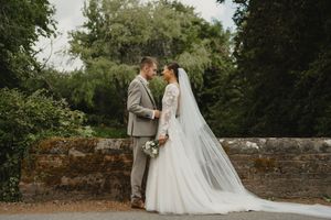 Romantic wedding couple poses in front of a rustic stone wall and lush greenery.