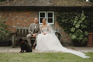 Elegant wedding couple shares an intimate moment on a stone bench near a brick building.