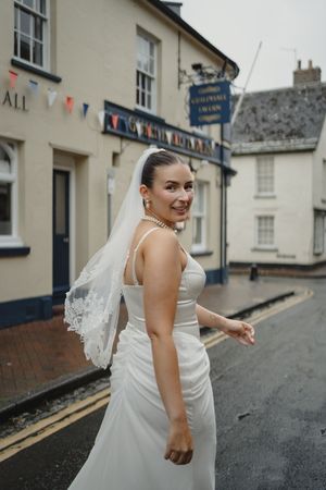 Bride in flowing white dress walking down a quaint village street.