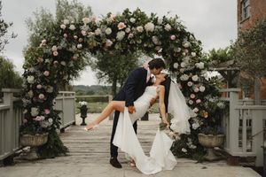 Wedding couple shares a romantic moment under a floral arch with pink roses.