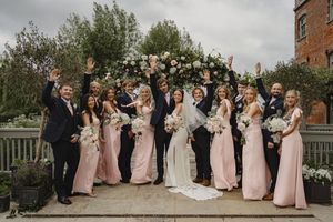 Wedding party in pink dresses poses for formal photos outside a brick building.