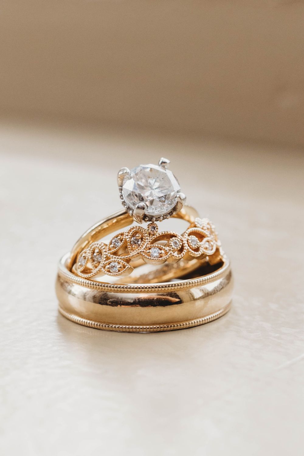 Gold wedding ring set featuring diamond solitaire and intricate leaf design bands on beige surface.