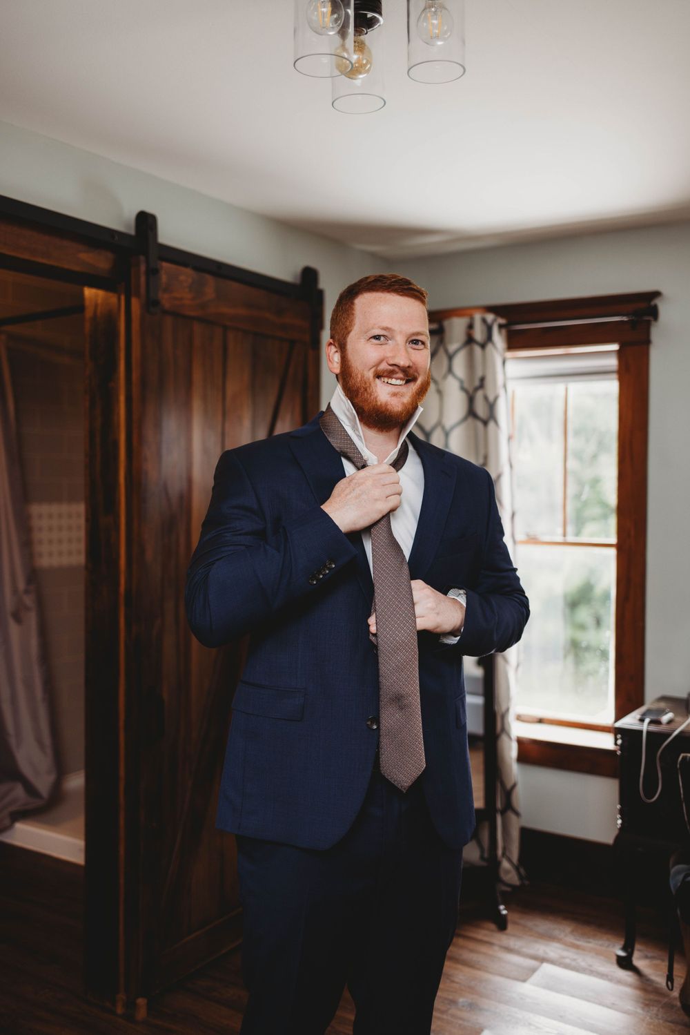 Someone adjusting their tie while getting ready in a room with wooden barn doors.