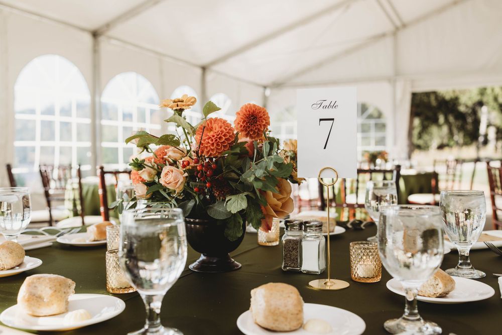 Wedding table setting with black vase floral centerpiece and place settings under white tent.