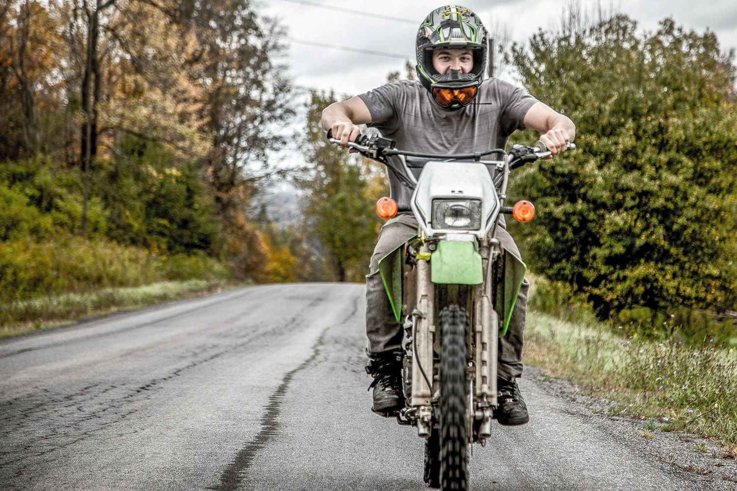 Motorcyclist riding dirt bike on wet rural road during autumn season.