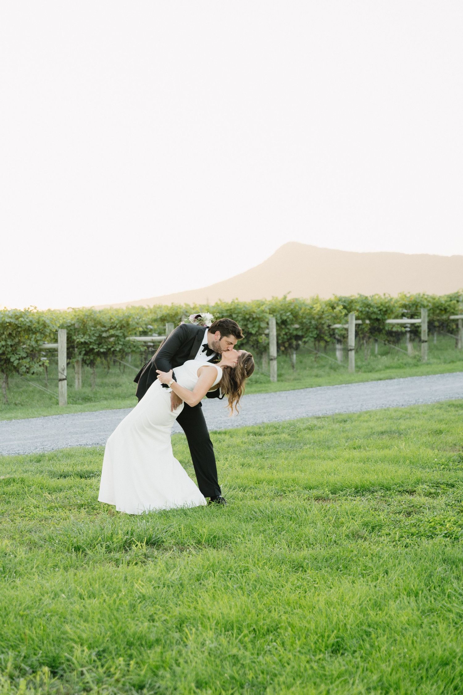 Romantic dip kiss between newlyweds in front of vineyard landscape.