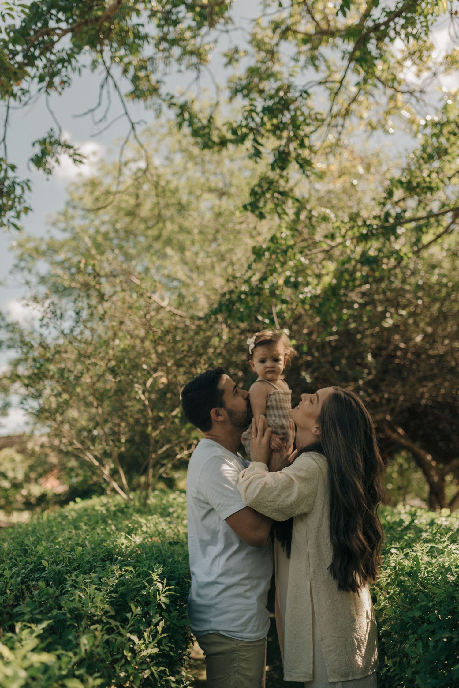 Family shares an intimate outdoor moment together among green foliage.