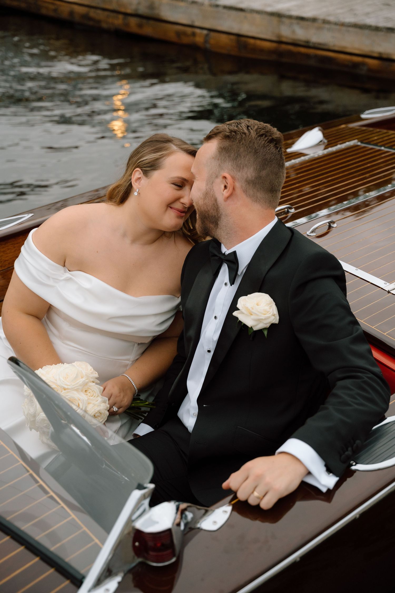 Newlyweds sharing intimate moment on wooden boat dock at sunset.