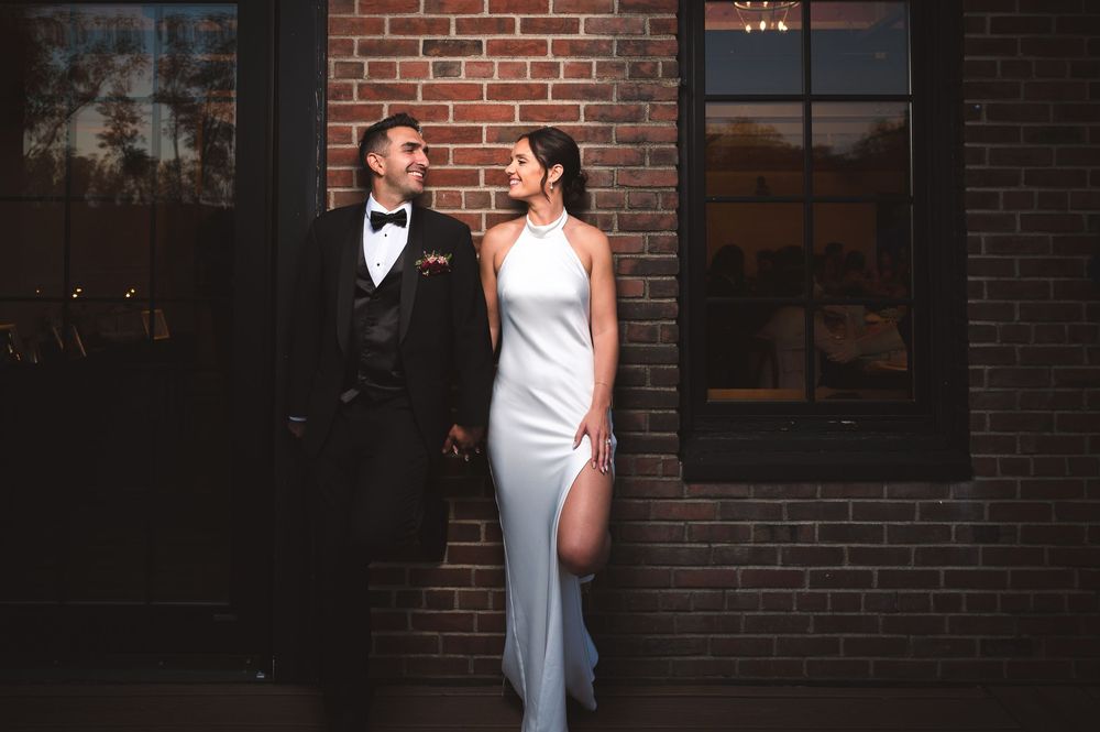 Elegant wedding couple poses together against rustic brick wall during evening photoshoot at Drowned Lands Brewery in Warwick, NY.