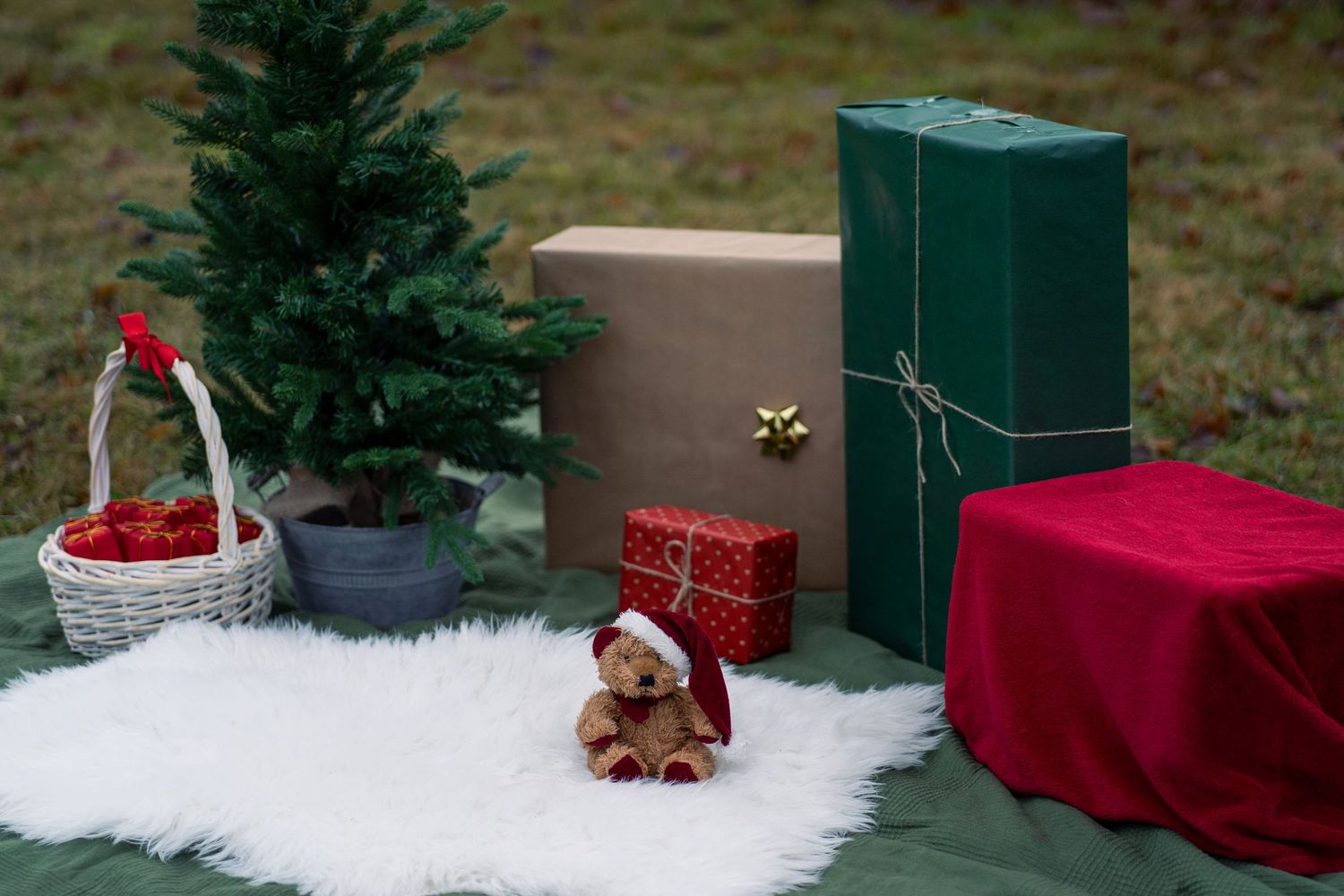 Holiday scene with mini Christmas tree, wrapped presents, and teddy bear on white fur.
