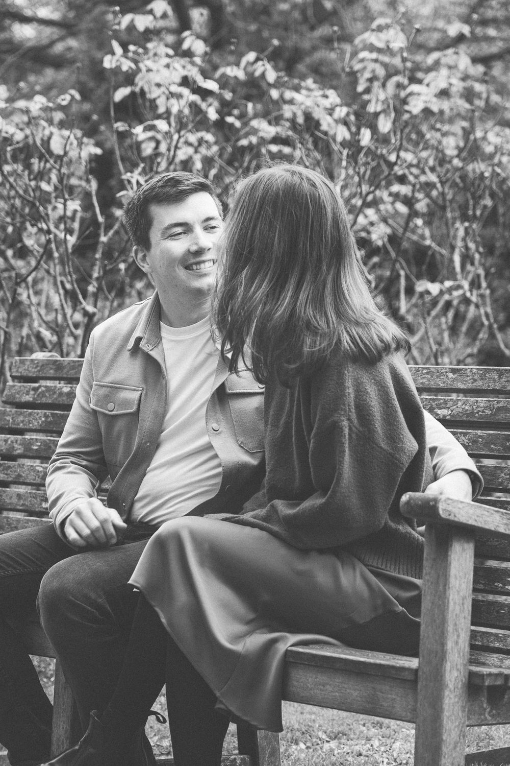 A couple sitting on a wooden bench sharing joyful moments in black and white.