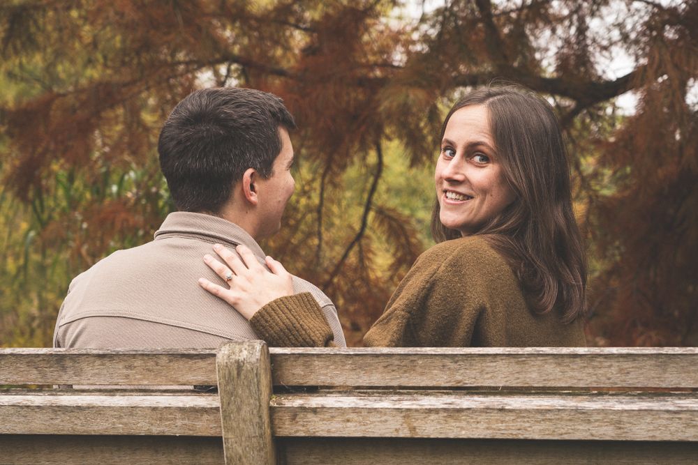 A couple sharing tender moments on a wooden bench in an autumn garden.