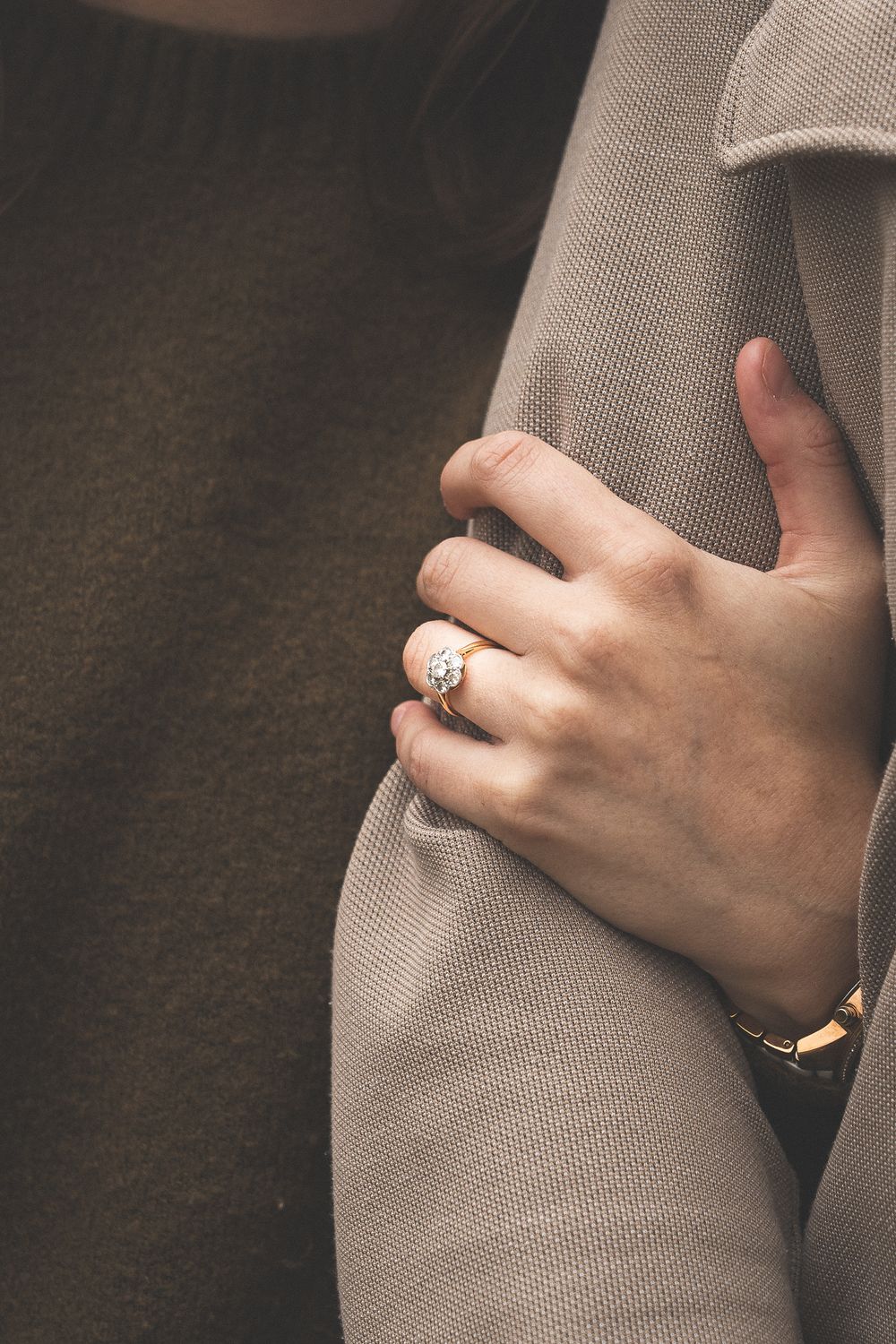Close-up of a hand wearing an engagement ring against a neutral background.