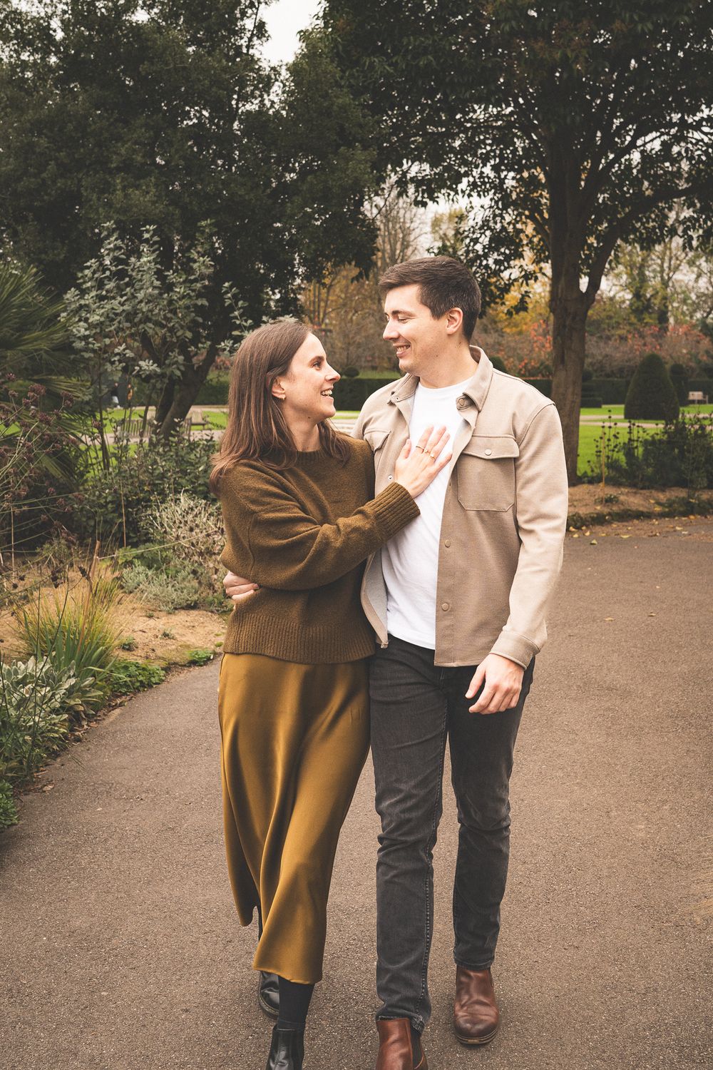 A playful couple laughing and embracing on a garden path during autumn.