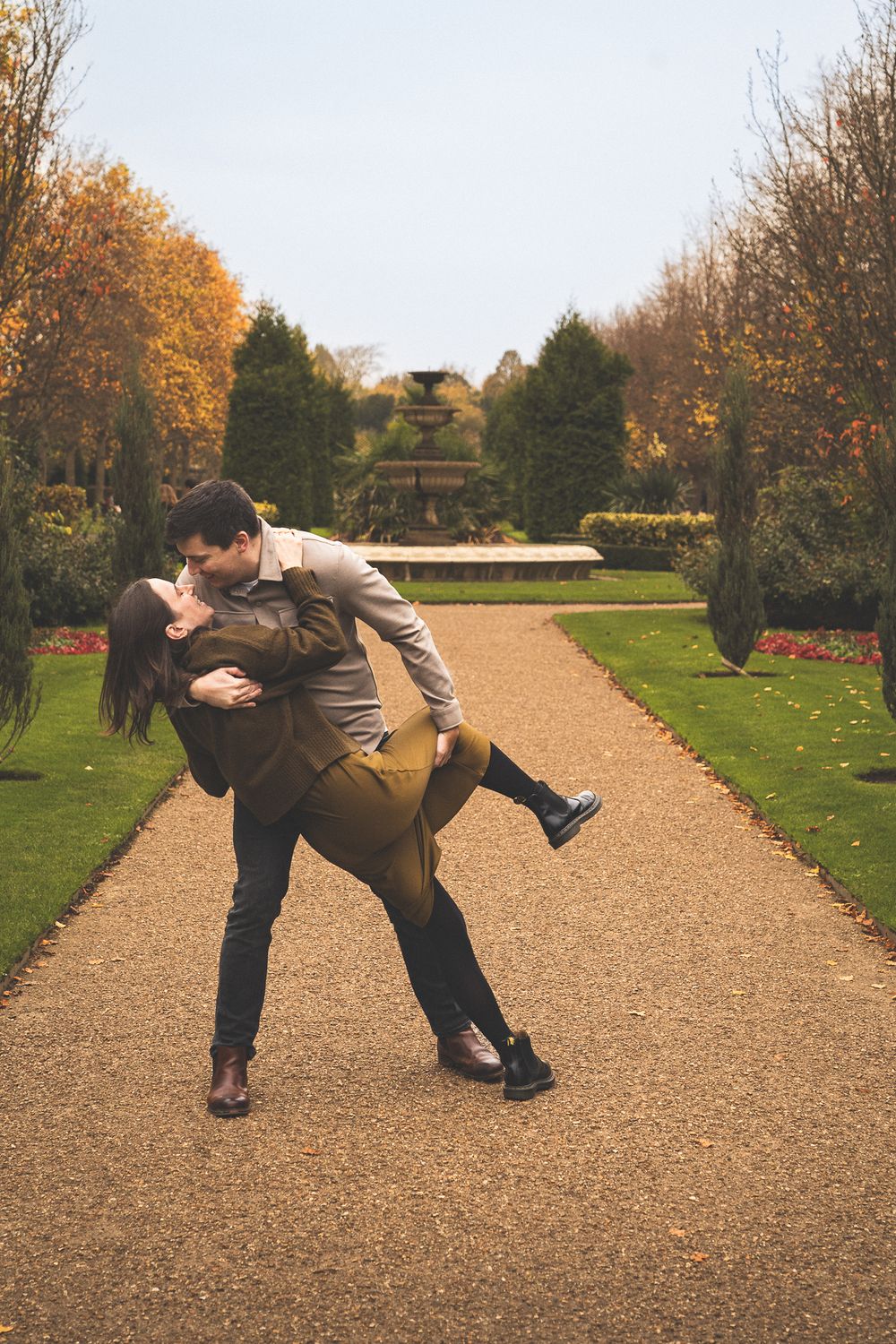 Couple performs dramatic dance-like dips on a garden path during fall season.
