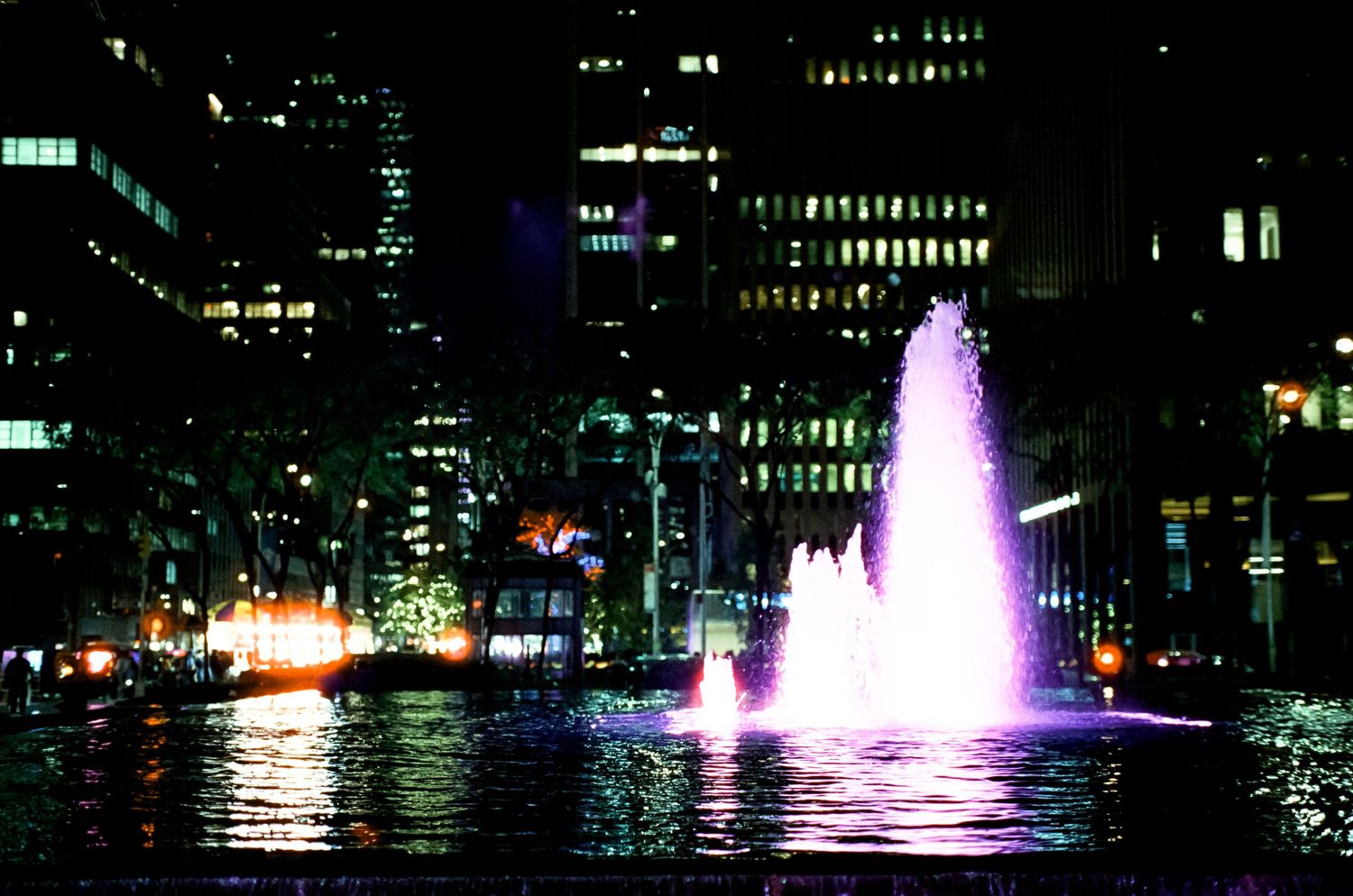 Purple illuminated fountain display in an urban plaza at night.