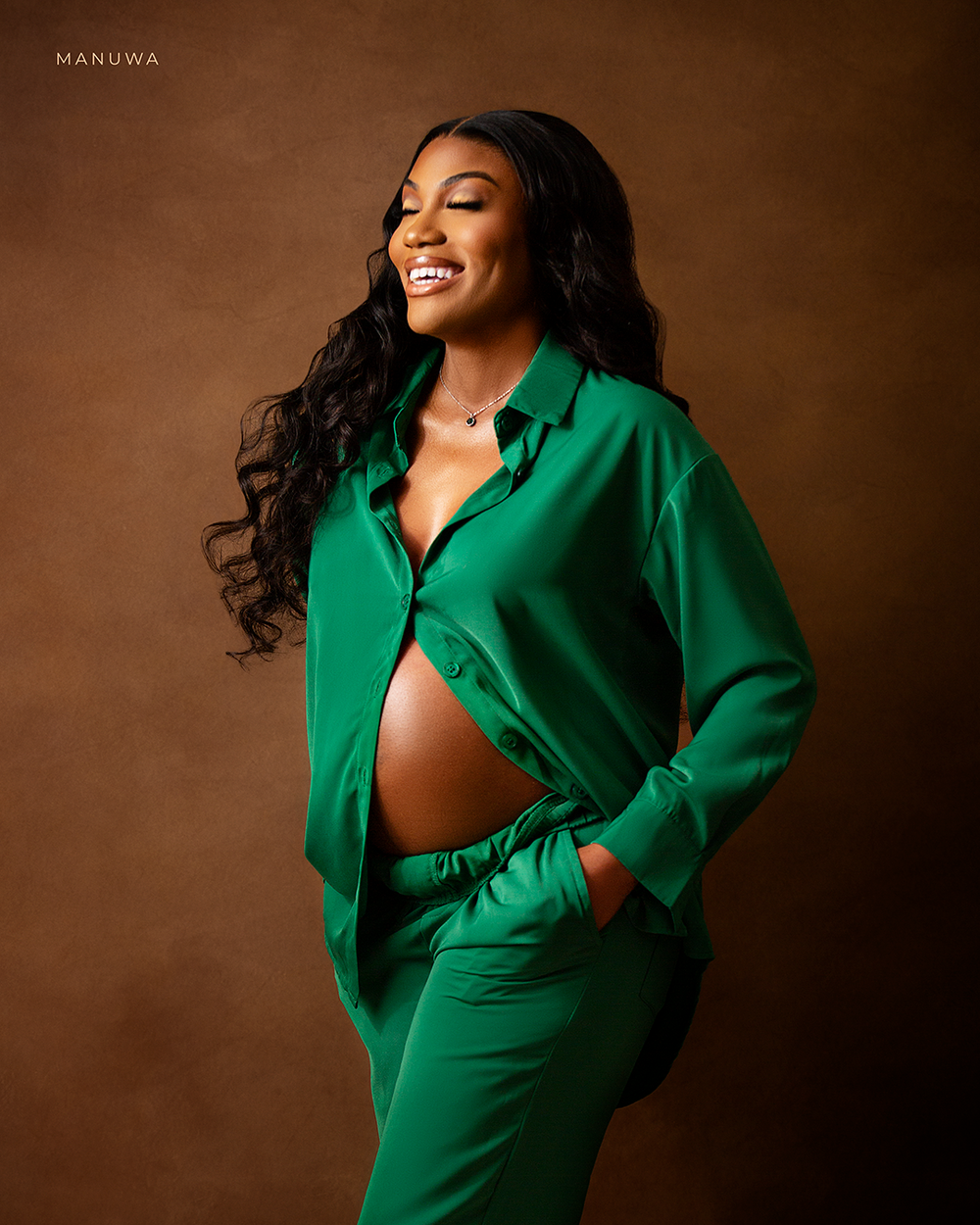 Maternity portrait of woman in emerald green pantsuit against brown backdrop.