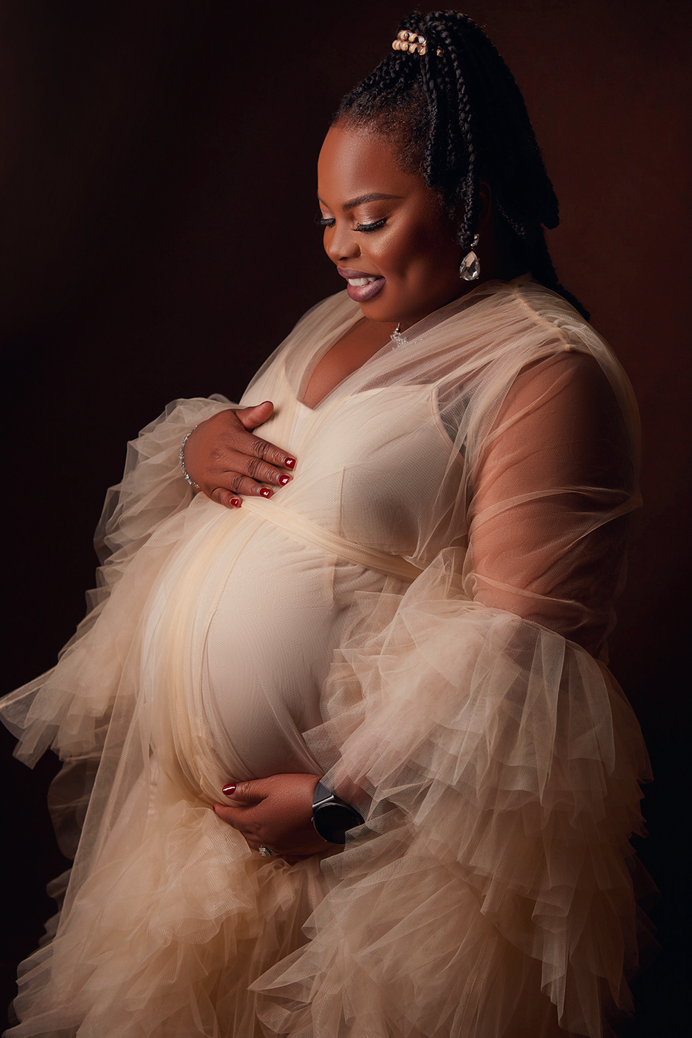 Soft ethereal maternity portrait featuring sheer tulle gown and delicate lighting against dark background.