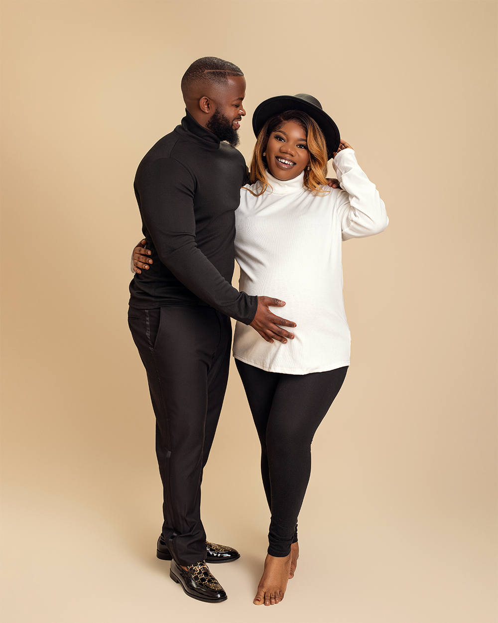 A couple in black and white outfits share a joyful intimate moment against a beige background.