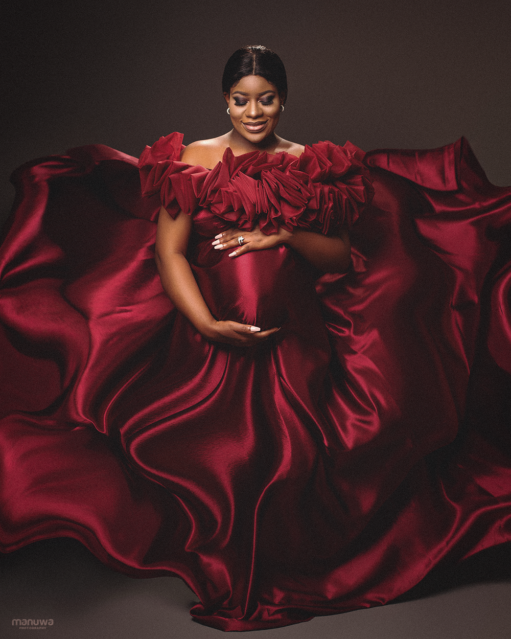 Dramatic maternity portrait in flowing red gown with ruffled details.