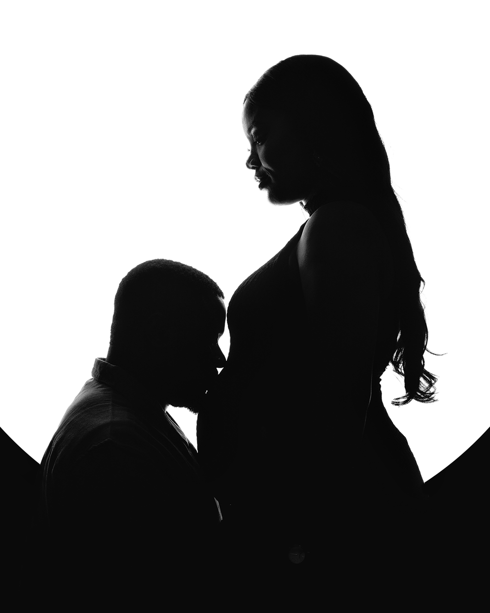 Black and white silhouette of a pregnant woman standing as another person kneels beside her in a tender moment.