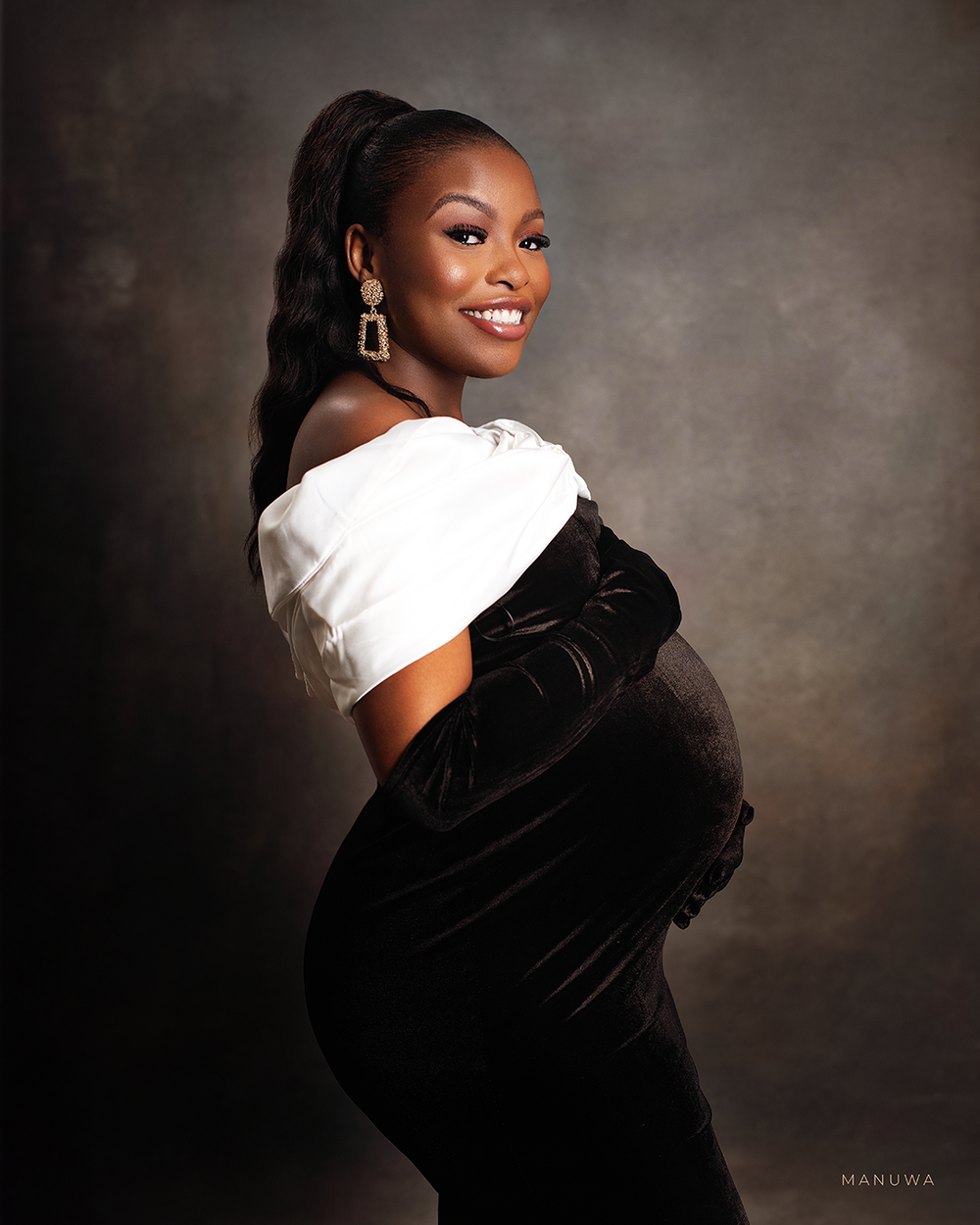 Stylish maternity portrait featuring black velvet dress and white top against neutral backdrop.