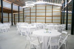 Large indoor reception venue with white folding chairs and round tables set up.