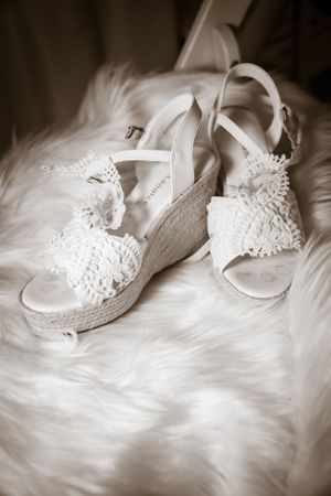 White lace bridal shoes with delicate floral details on a soft textured background.