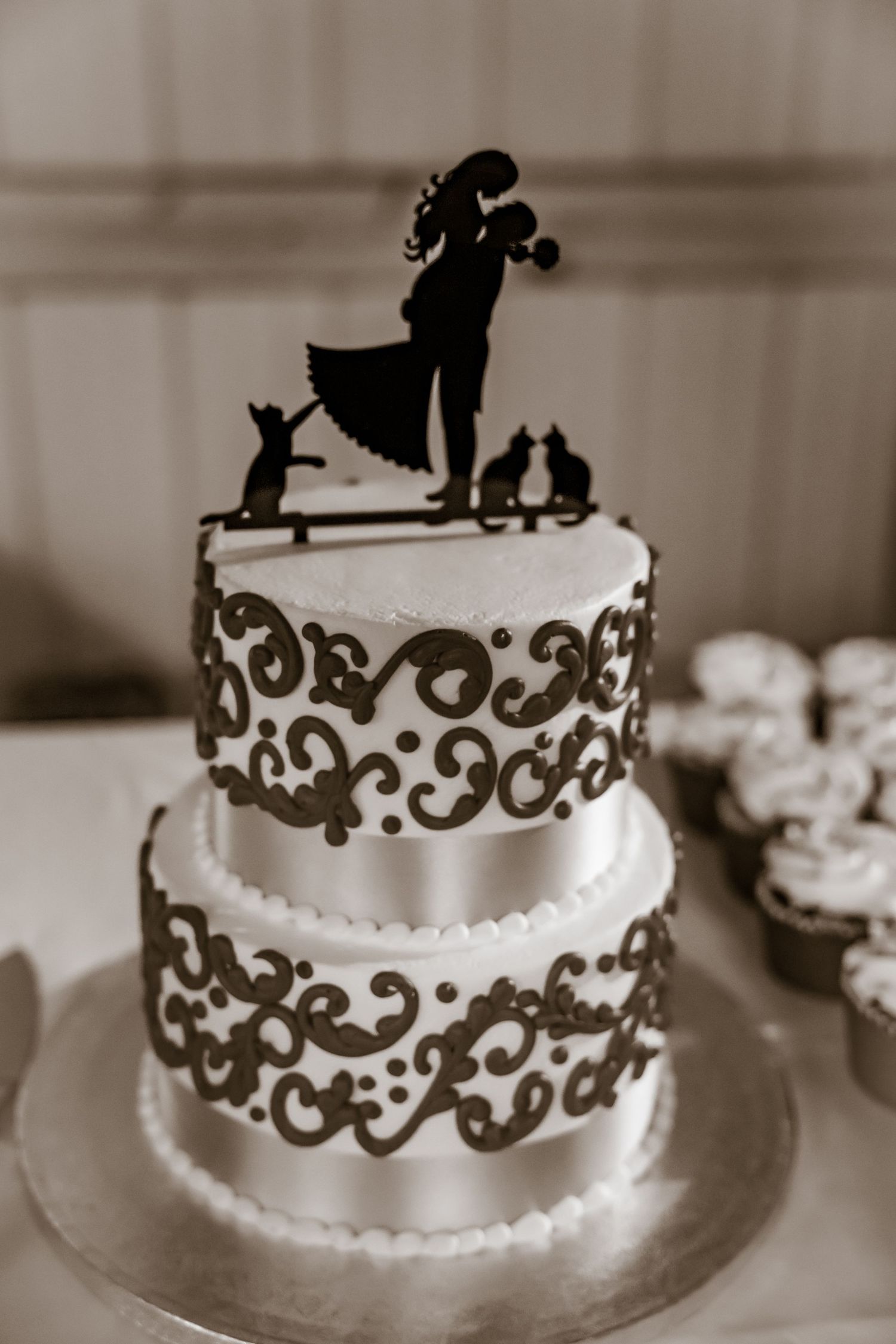 White wedding cake with elegant brown scrollwork details and silhouette topper.