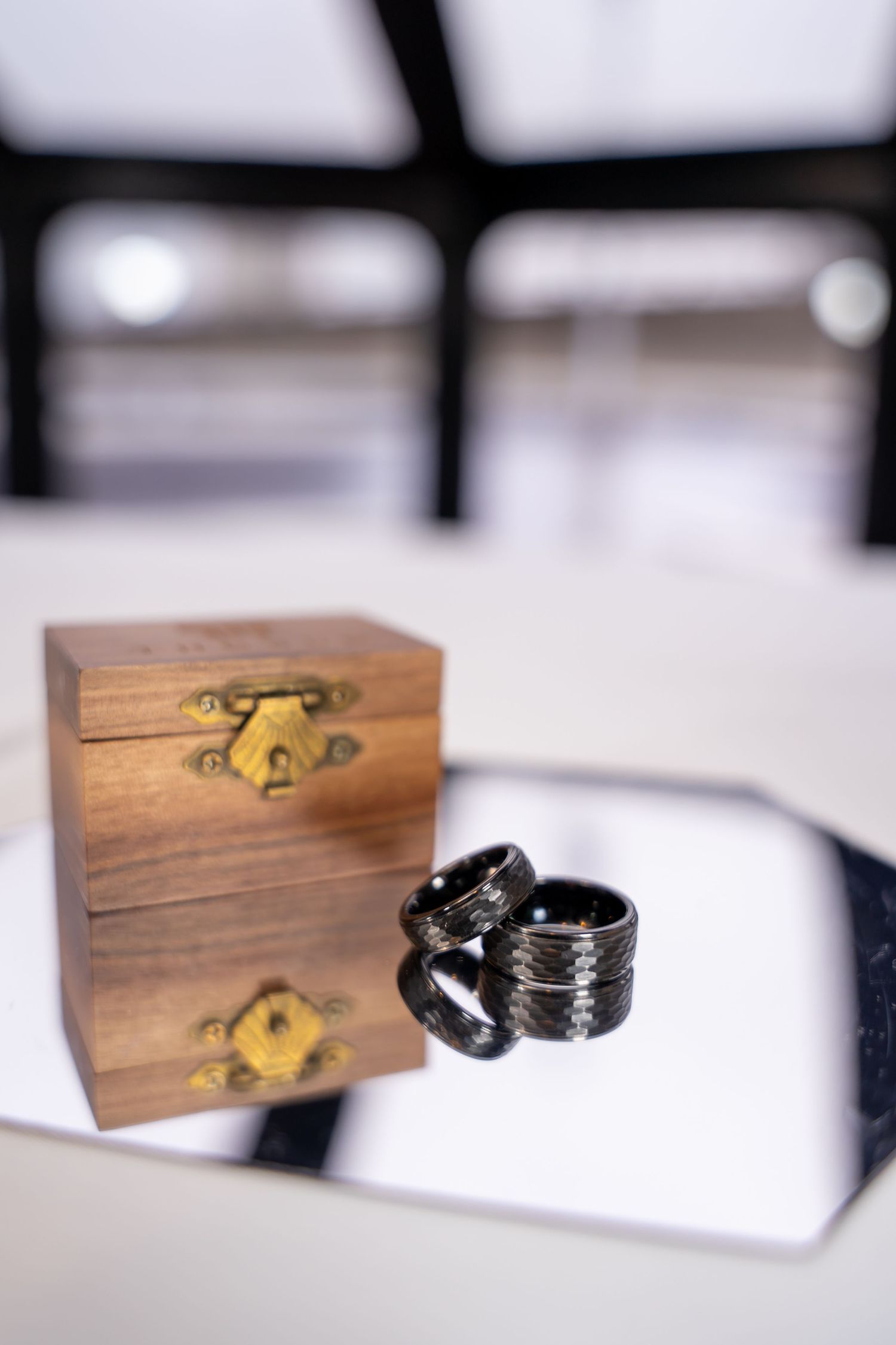 Small wooden ring box with brass latch and black wedding rings displayed against white background.