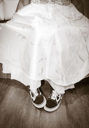 White sneakers peek out from under a flowing wedding dress on wooden flooring.