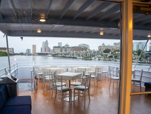Spacious waterfront restaurant interior with white tables and chairs overlooking a harbor view.