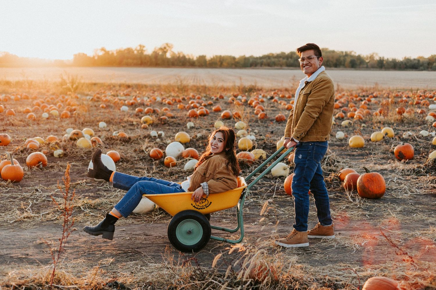 couple pushing each other on hay barrel at the pumpkin patch