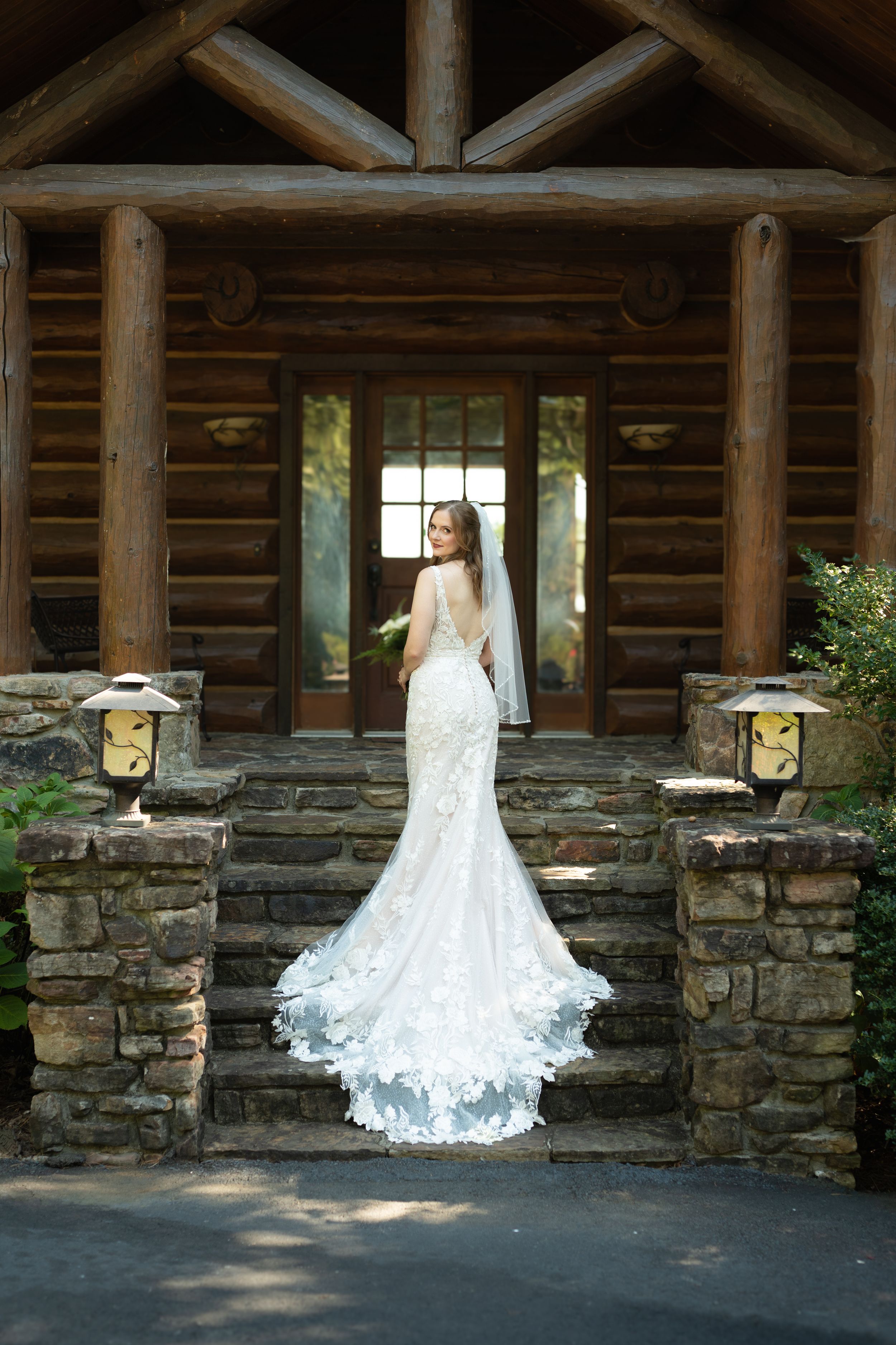 Bridal portrait against rustic log cabin with stone foundation in natural lighting.