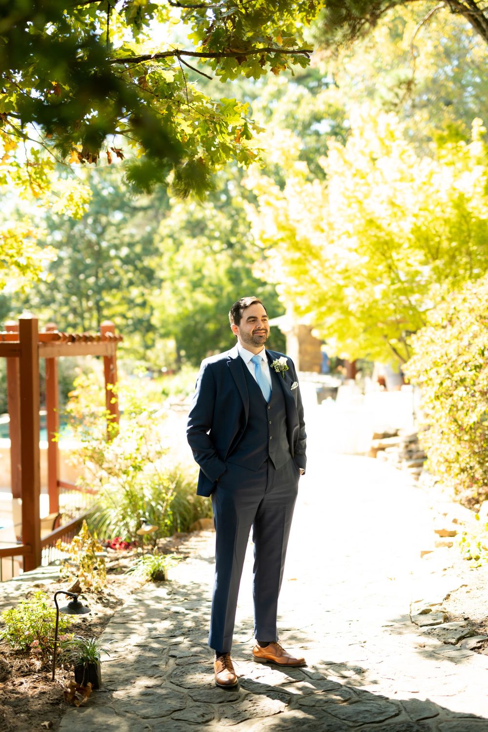 Groomsmen in navy suits standing in dappled sunlight on a garden path.