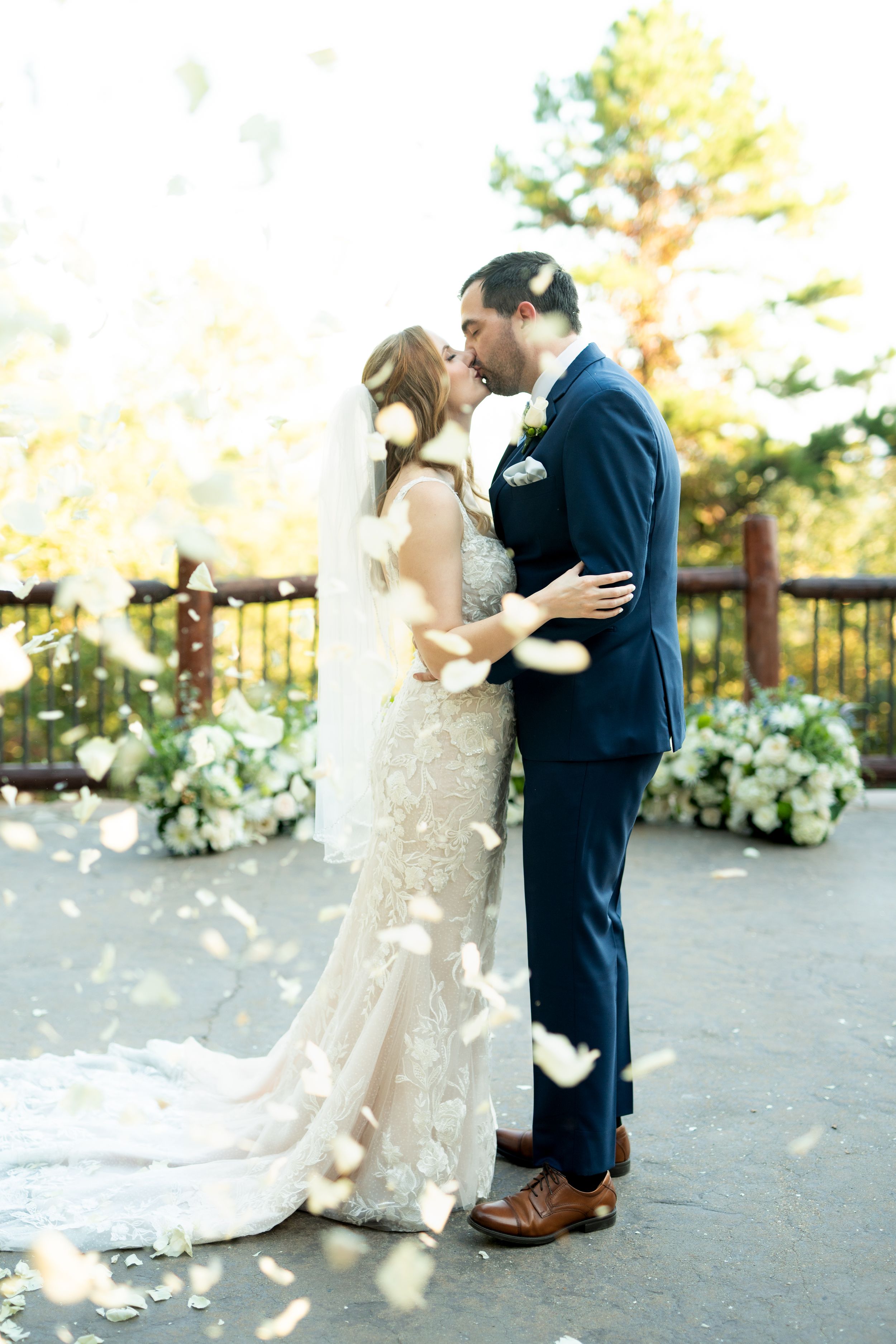 Romantic wedding couple embracing outdoors in front of white floral decorations.