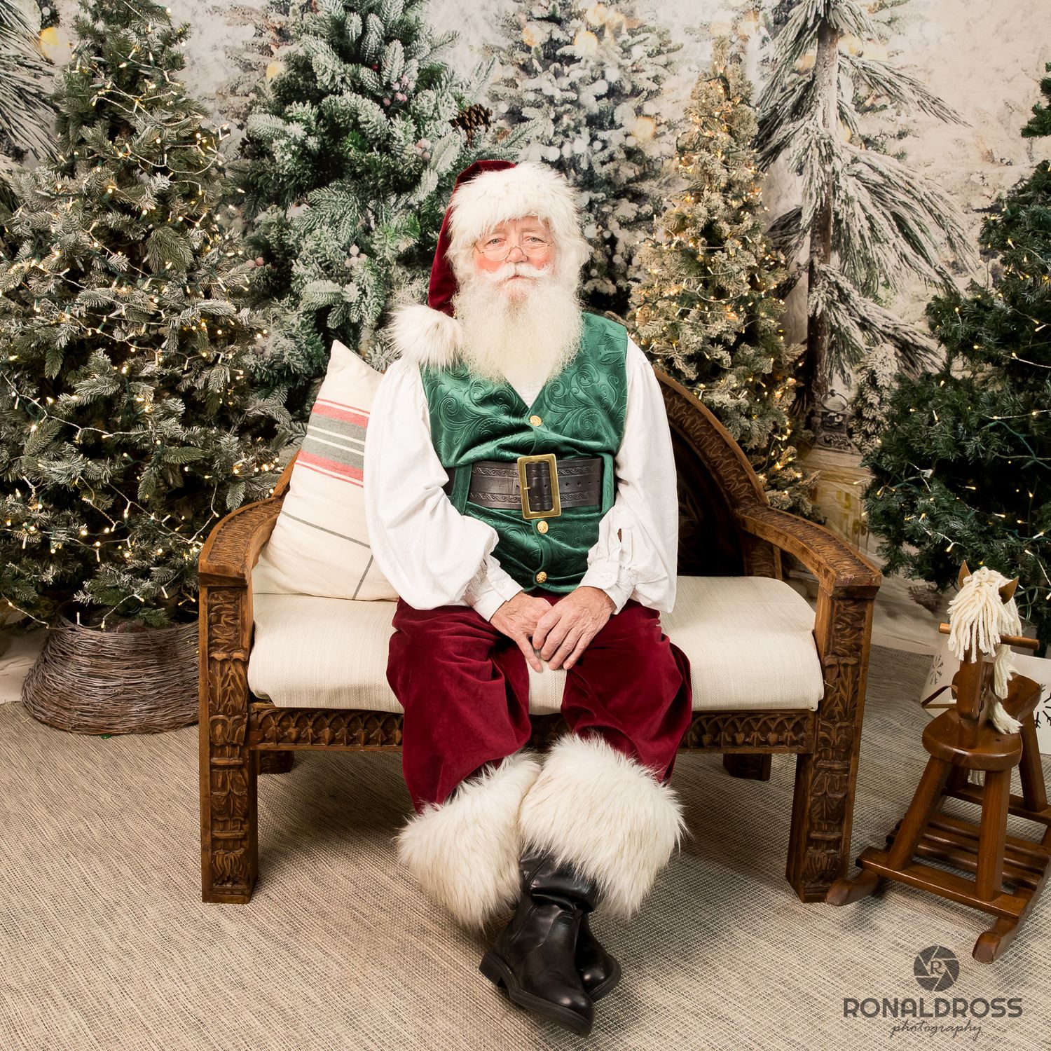 Santa Claus seated on wooden bench with snowy Christmas trees in background. Santa Photos Webster League City Galveston