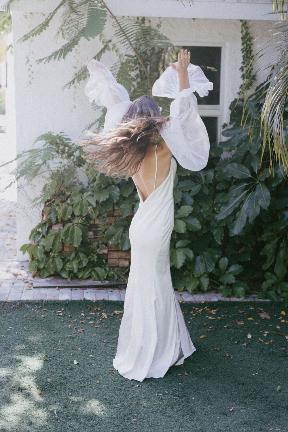 Woman in flowing white dress dancing with hair in motion against tropical foliage.