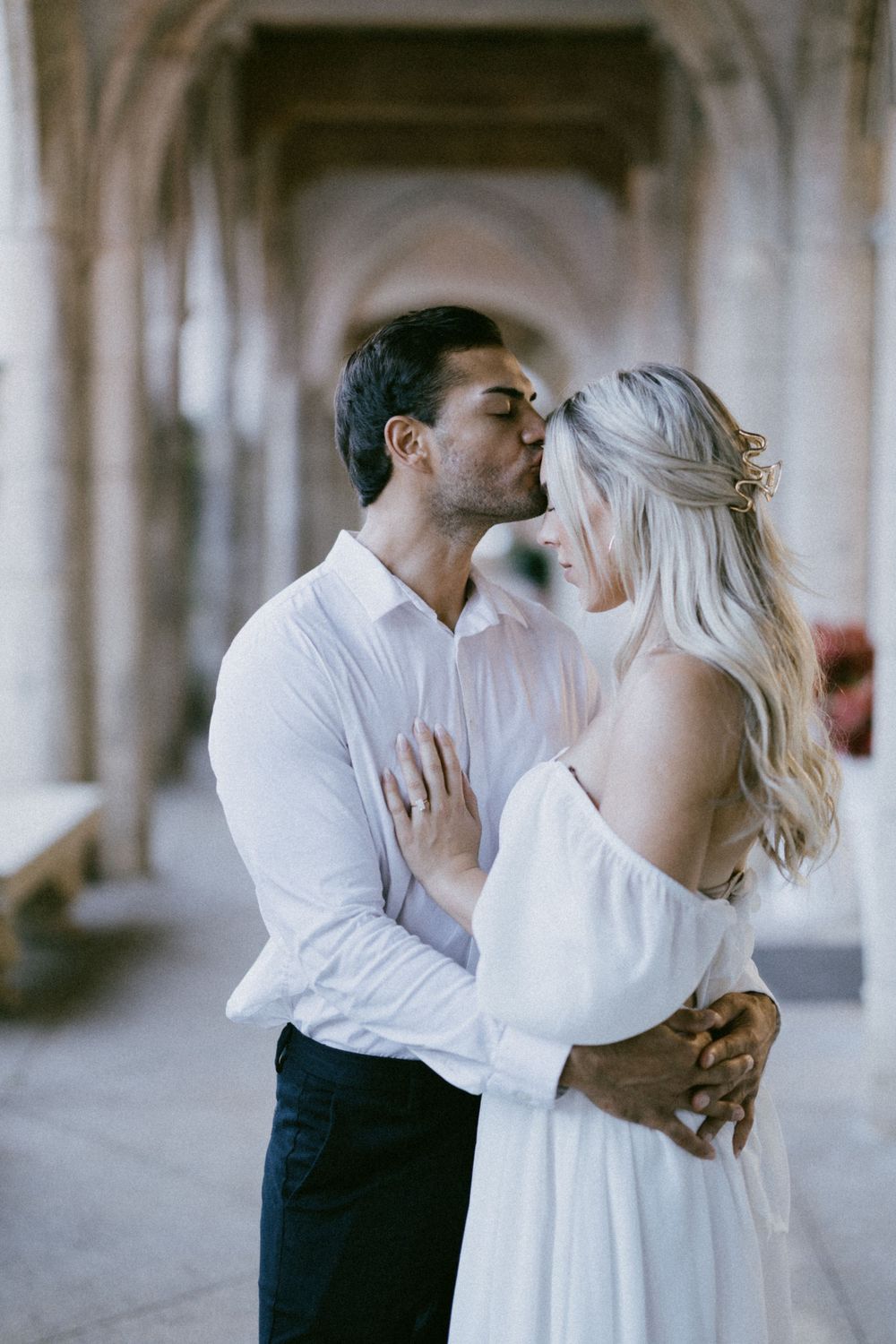 Romantic couple sharing a tender moment in an elegant colonnade hallway.