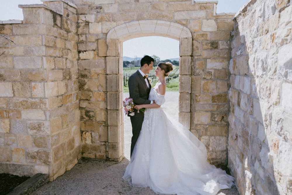 Wedding couple stands in stone archway with countryside views in background.