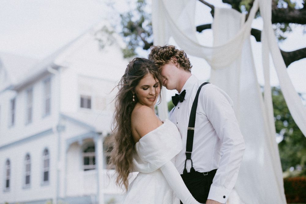 A romantic moment shared between newlyweds against a white building backdrop.
