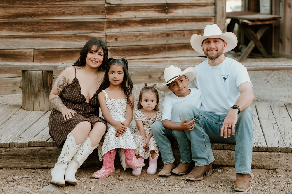 Family of five posing together on rustic wooden steps, wearing western attire including cowboy hats and boots.