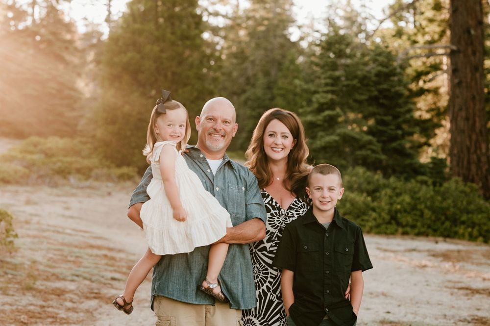 A family of four poses together on a sunny forest trail during golden hour sunset.