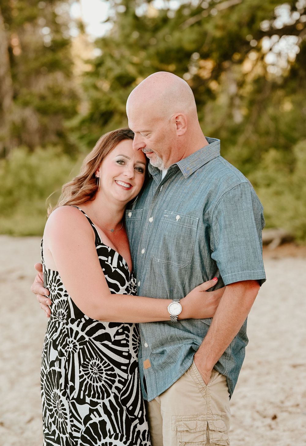 A couple shares tender moments outdoors during a sunset photography session wearing a blue shirt and patterned dress.
