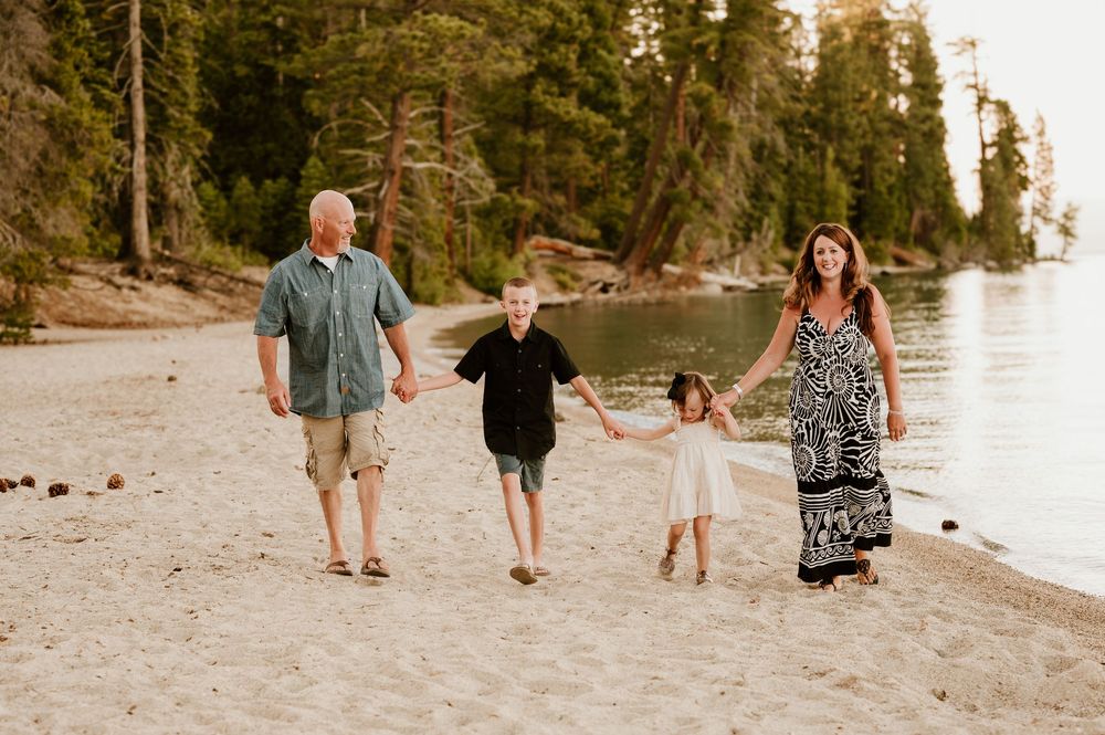 A group walks hand in hand on a peaceful lakeside beach with tall pine trees in the background at sunset. Tahoe beach photographer