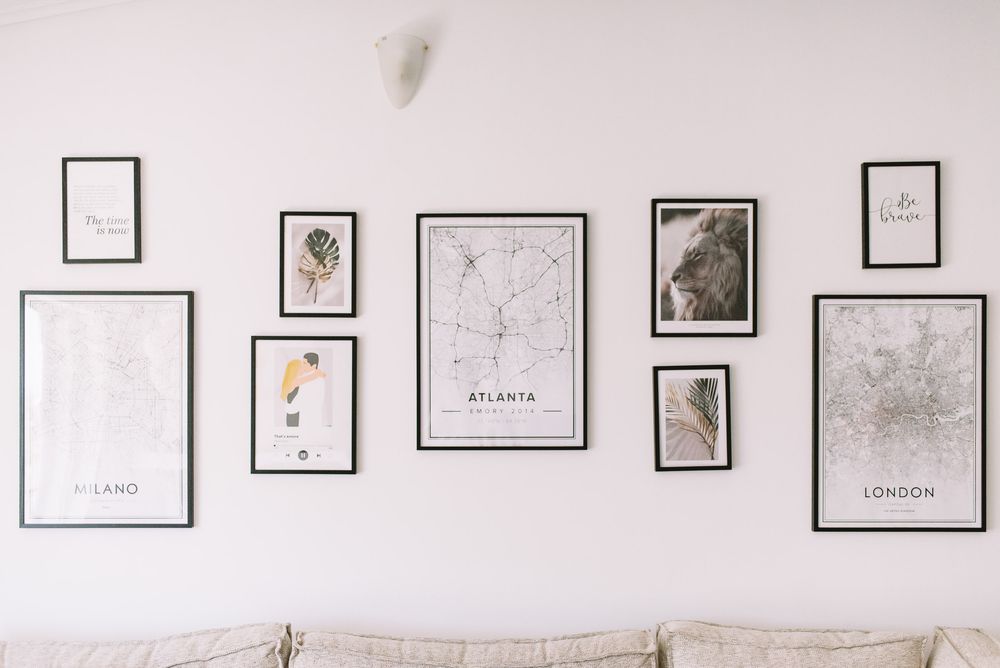 Minimalist gallery wall with black and white city maps and art prints arranged above a light colored sofa.