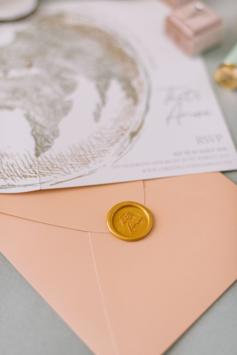 Peach colored envelope sealed with a gold wax stamp sits beside a delicate paper with floral designs.